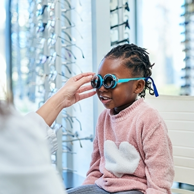 Young black girl in a pink shirt tries on aqua blue glasses