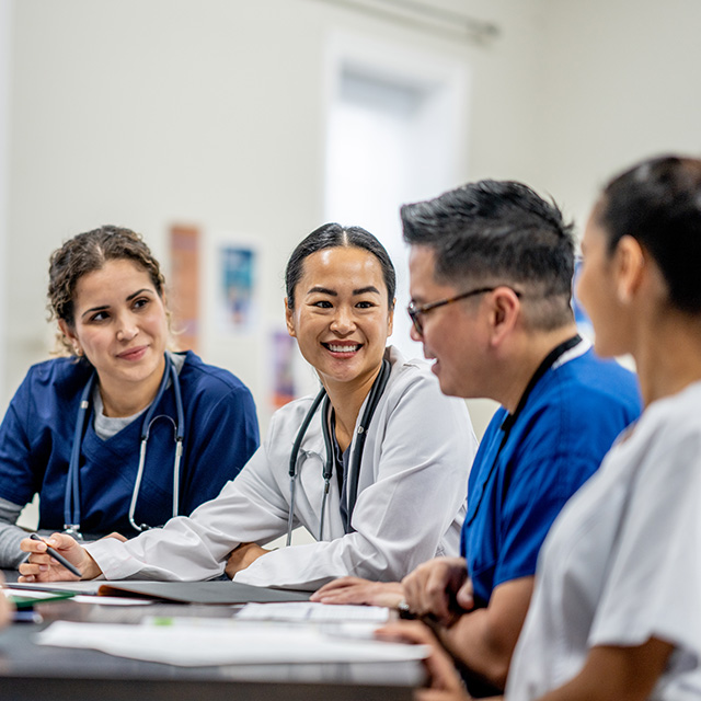 A group of doctors engaged in discussion around a conference table, with medical charts and laptops in front of them.