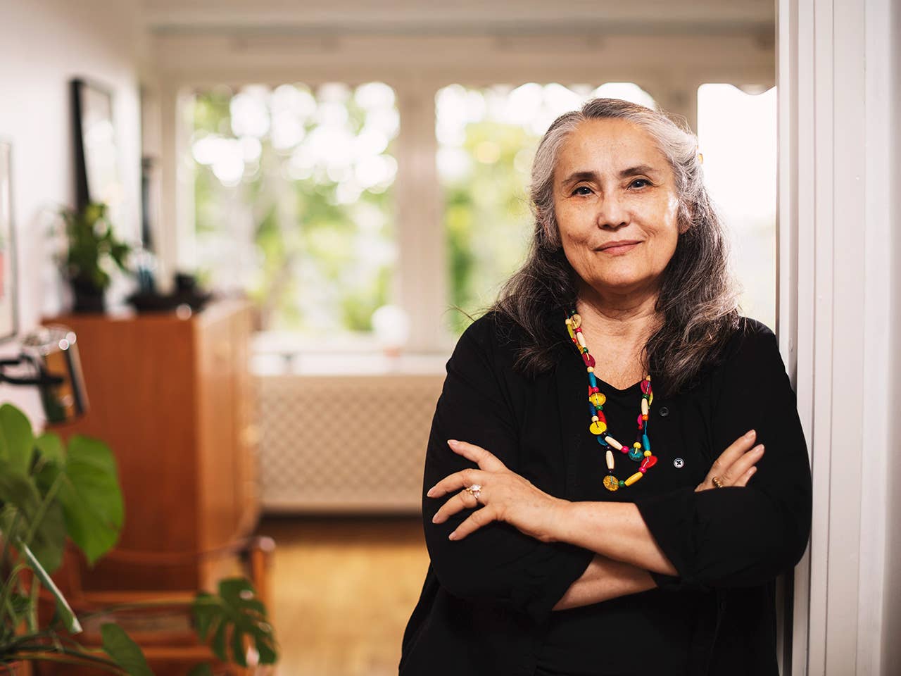 White woman wearing a black blouse leans against a wall crossing her arms