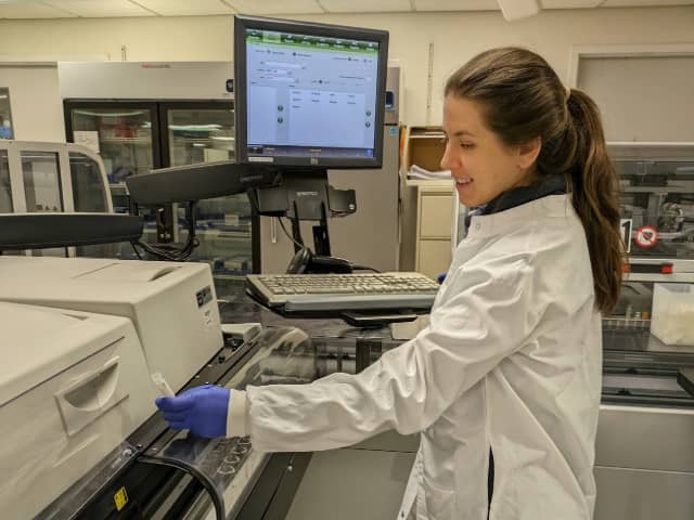 A woman wearing a lab coat presents a tray, indicating a hands-on approach to her research or project.