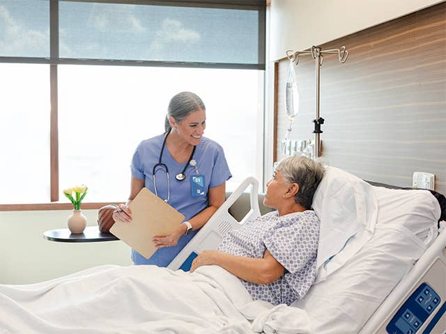 Hospital worker standing at the bedside of a patient and talking