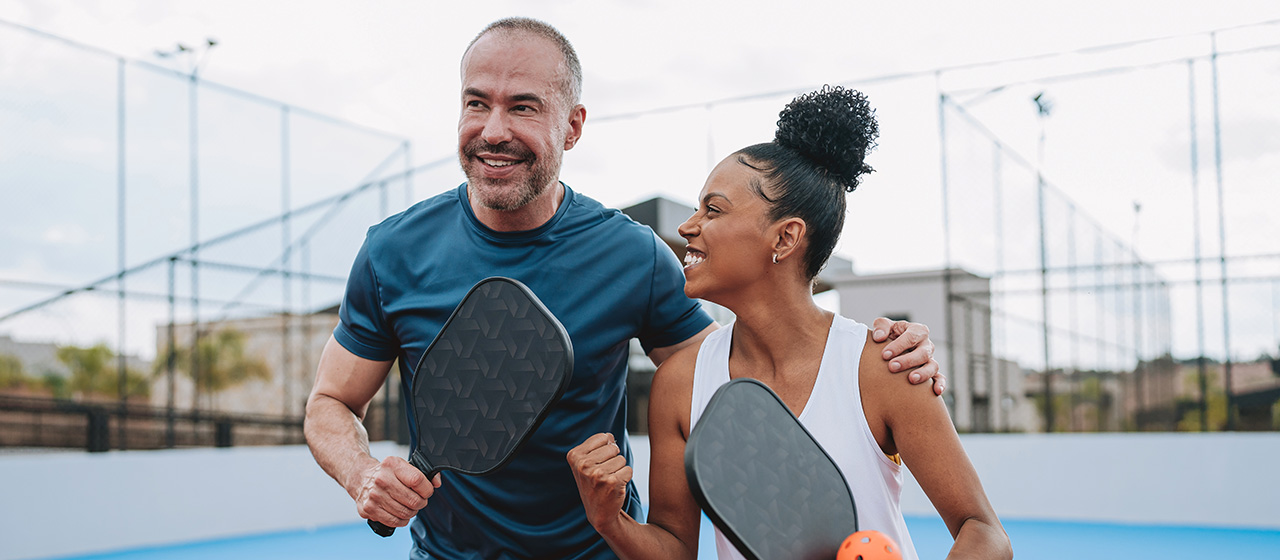 Two people holding pickleball paddles on an outdoor court, highlighting an active lifestyle supported by healthy nutrition.