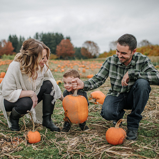 A family enjoying a day at a pumpkin patch, surrounded by pumpkins and vibrant autumn foliage.