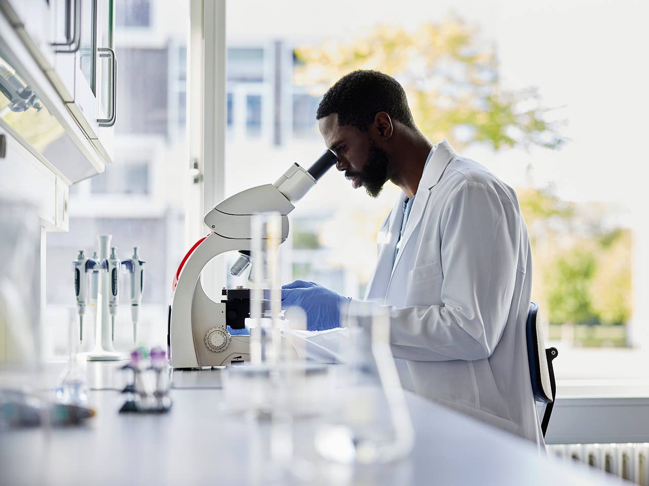 Corewell Health laboratory specialist wearing a white lab coat sitting at a desk and looking into a microscope
