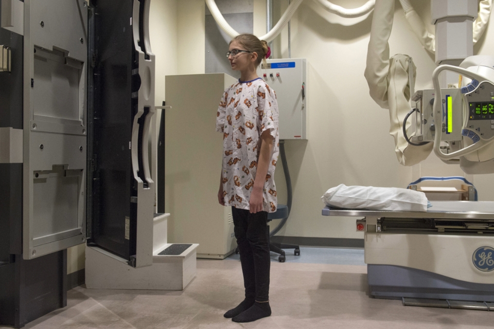 Teenage girl with glasses stands while getting an X-ray in the pediatric orthopedics clinic