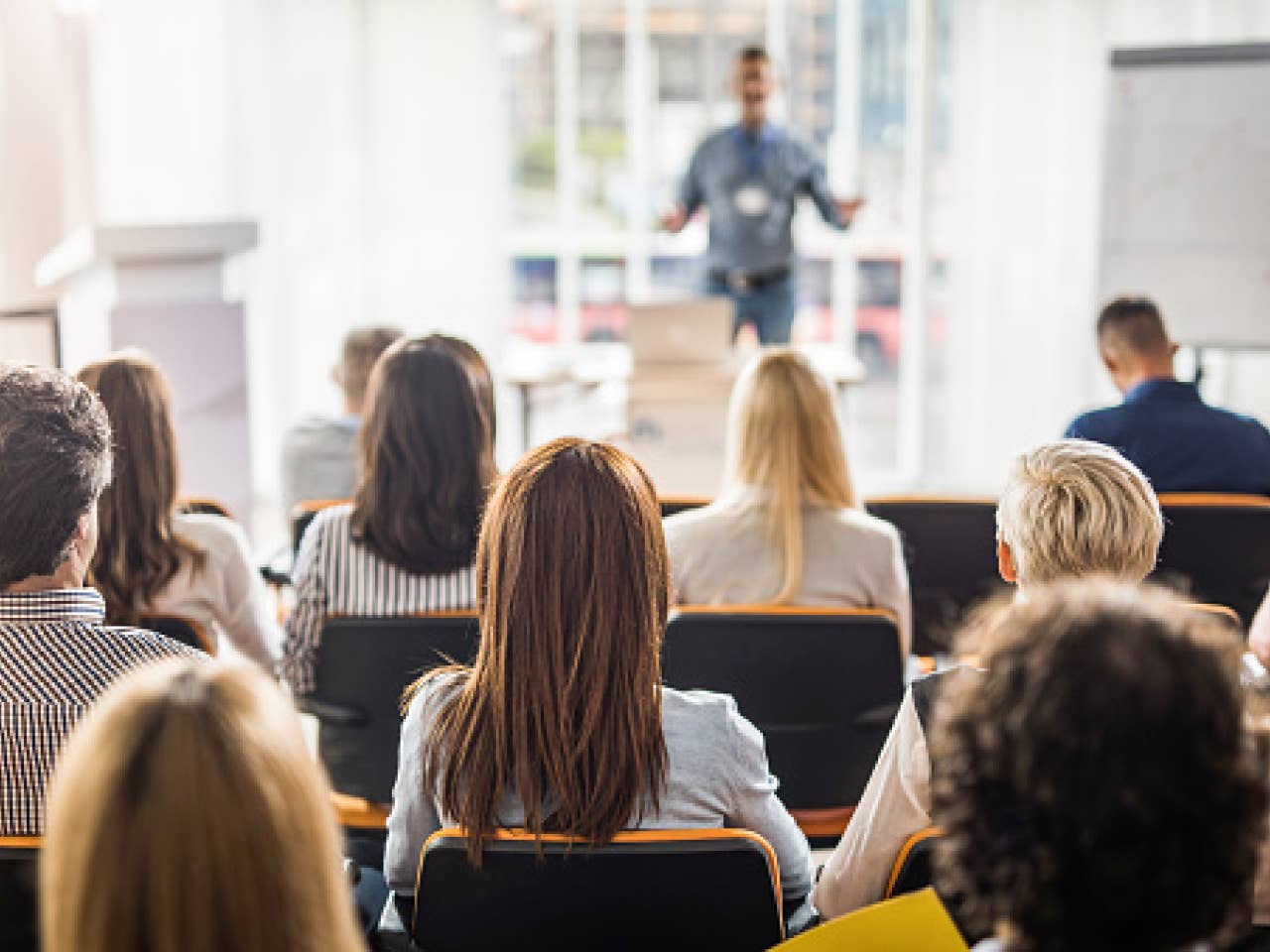 A man stands at a podium, presenting to an engaged audience seated in row.