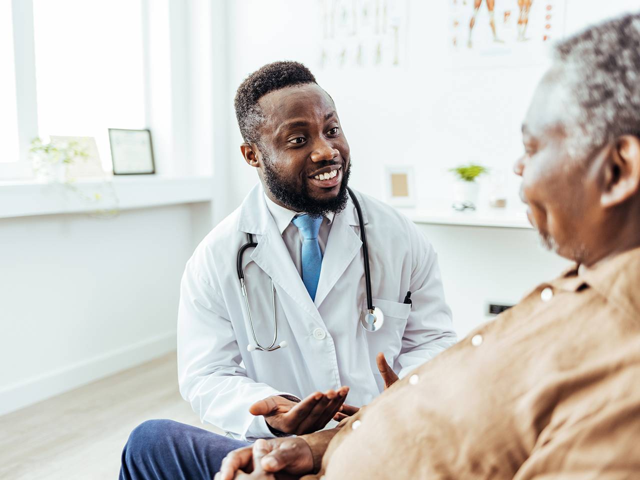 A male doctor converses with an older man in a medical office setting, discussing health concerns.