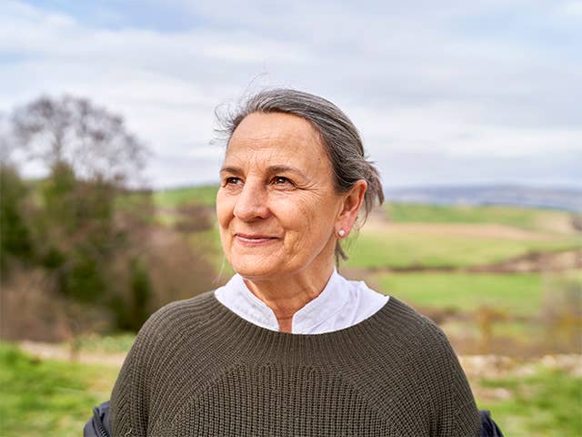 White woman with hair pulled back into a bun stands in a field outdoors