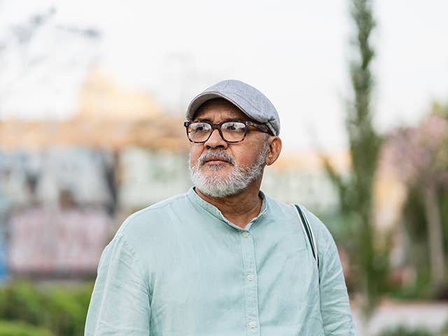 Older white man with glasses and a grey goatee stands outdoors in the evening sun