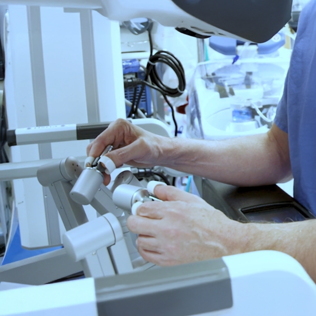 A person operates a robotic surgery console, manipulating controls with both hands.