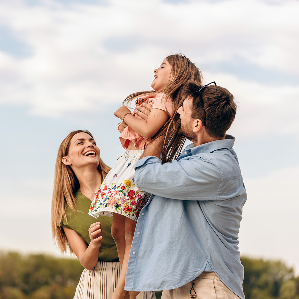 Smiling mom and dad lift their young daughter up