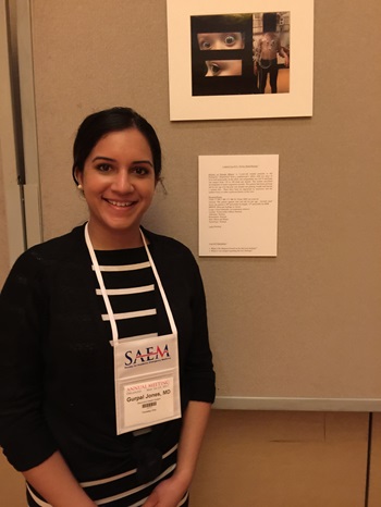 A woman stands adjacent to a poster with a woman's image, representing a focus on pediatric emergency medicine research initiatives.