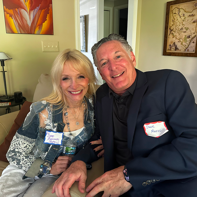 Two attendees seated together indoors at a social gathering, wearing name tags.