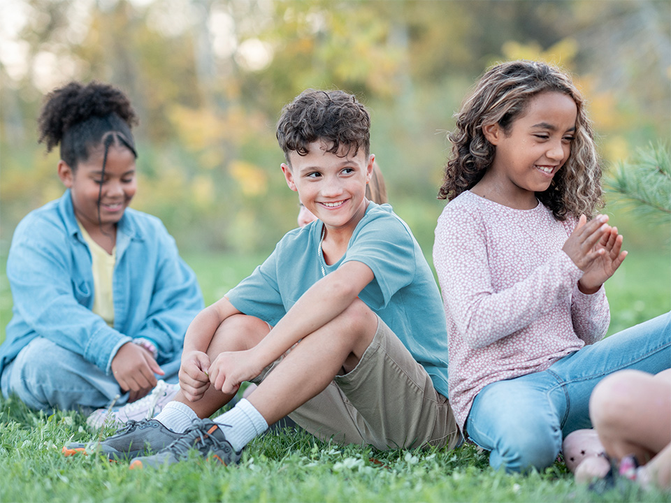 Three children seated on grass outdoors, interacting together in a park setting.