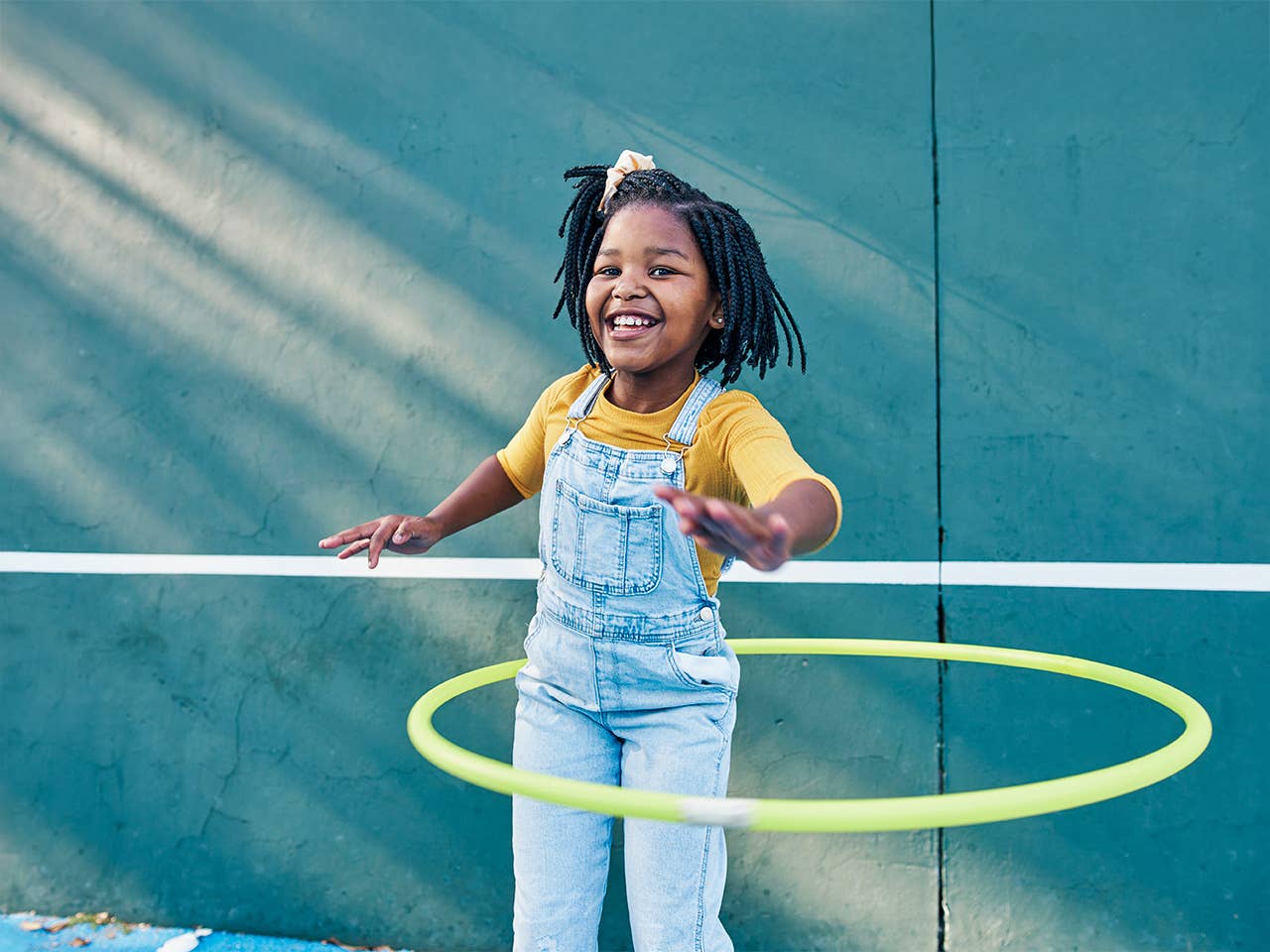 Young girl hula hopping outside at a park.