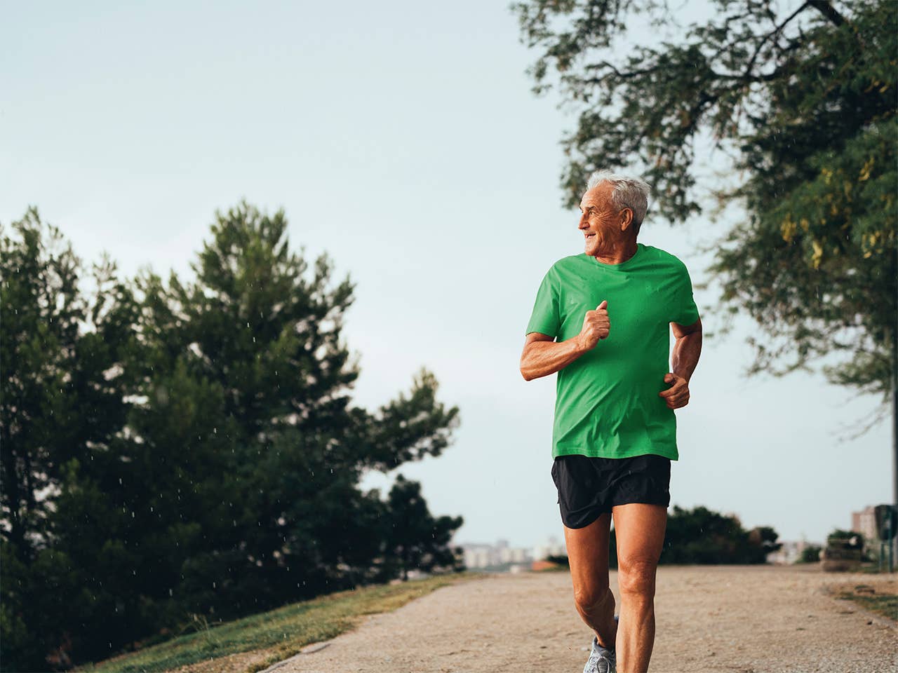 Older man wearing a green shirt runs down a paved path outdoors in the sunset