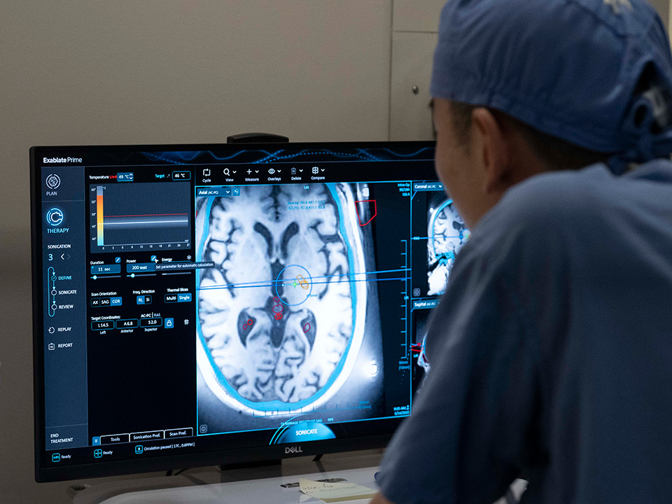 A man in a hospital room intently looks at a computer screen, surrounded by medical equipment.