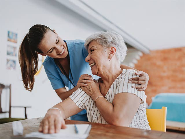 Smiling Corewell Health nurse places a hand on the shoulder for a patient as she sits at a table in her home
