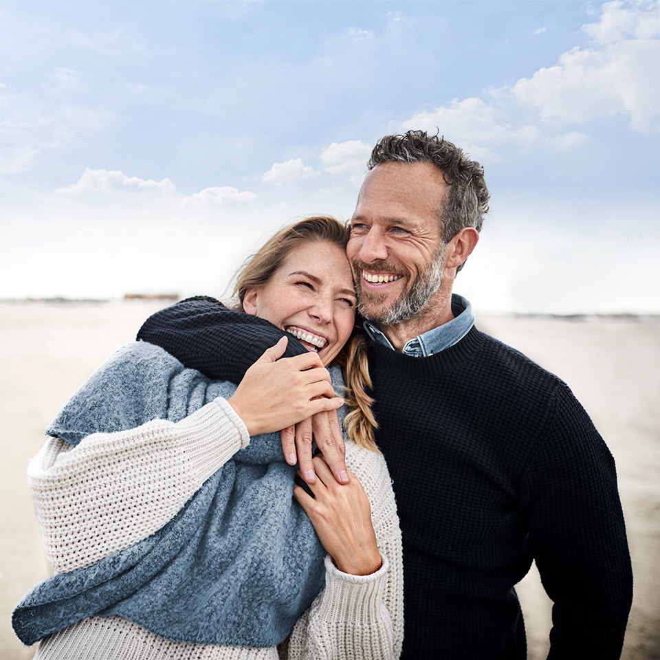 Smiling man and woman hug on a beach
