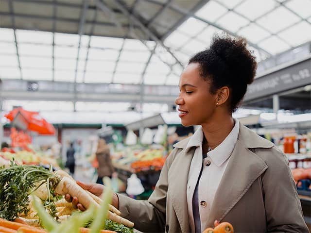 Person selecting fresh carrots and root vegetables at a market, finding healthy foods that fit a budget.