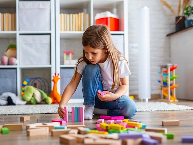 Girl wearing jeans and a white T-shirt plays with colorful blocks on a hardwood floor