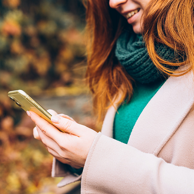 A smiling woman with red hair holds a cell phone.