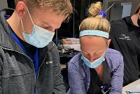 Individuals in masks and gloves engage in a collaborative project, highlighting safety measures in resident teaching.