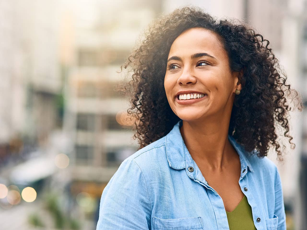 Smiling Black woman in a light blue blouse stands outdoors in a city
