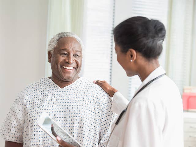 Smiling Black man wearing a medical gown speaks to his Corewell Health heart and vascular specialist