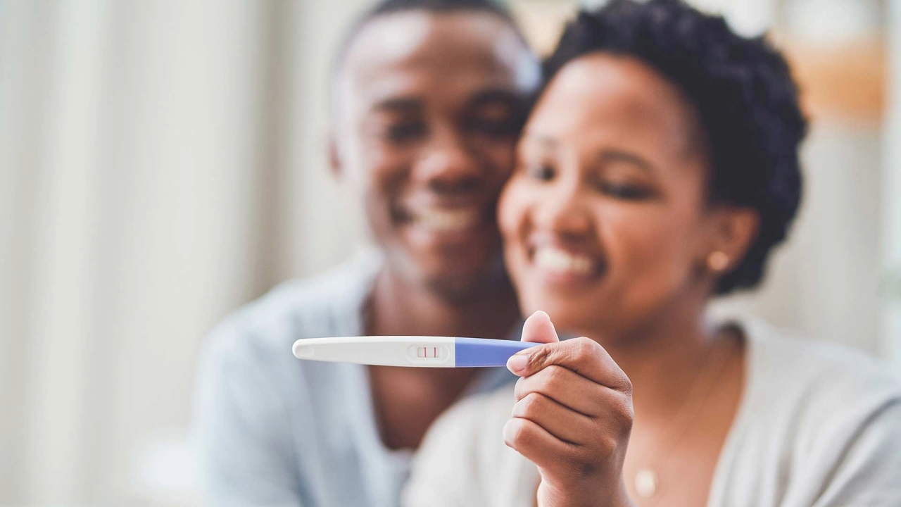 Smiling young Black man and woman look at a home pregnancy test which the woman is holding