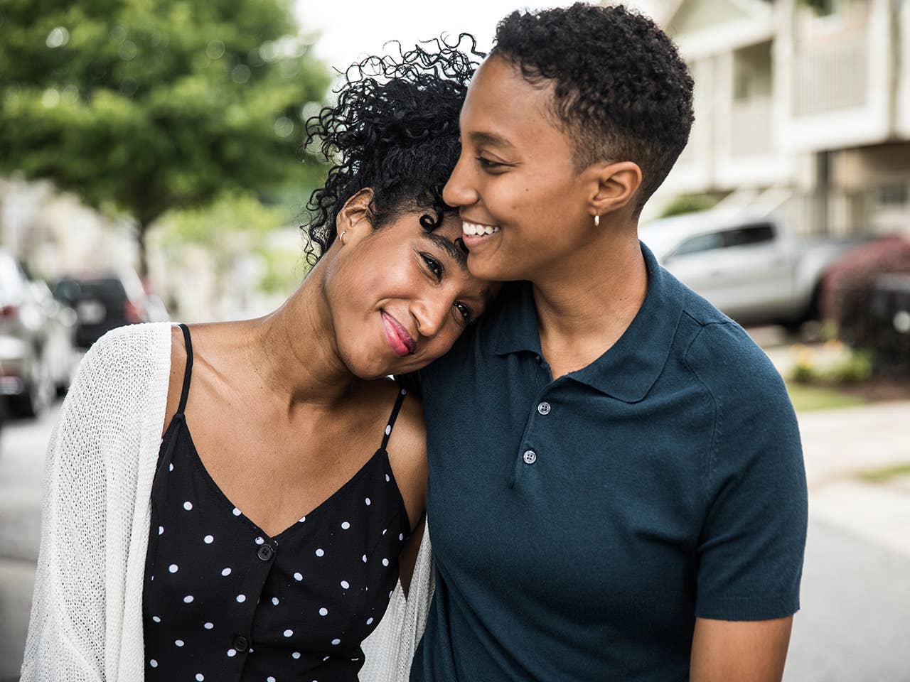Young Black woman smiles as she rests her head on the shoulder of her partner