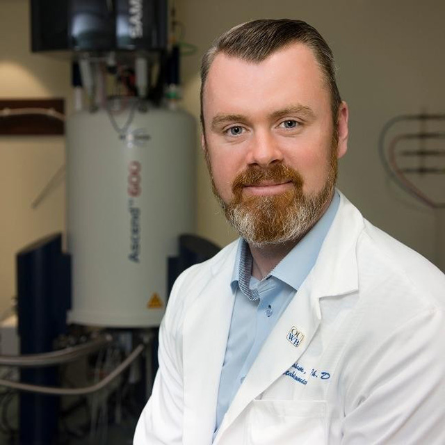 Stewart Graham, PhD, a white man with brown hair and a beard, wearing a white lab coat