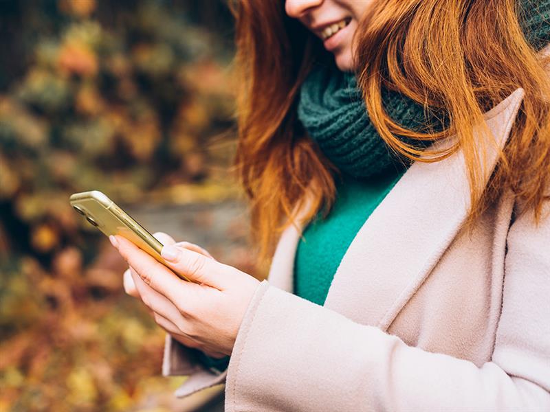 A smiling woman with red hair holds a cell phone.