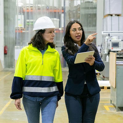 Woman in suit pointing while speaking with a woman in a hardhat and safety vest