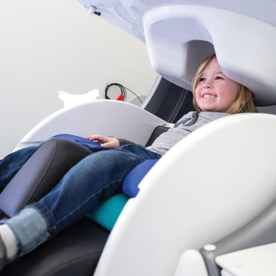 Smiling girl sits in a chair for a Magnetoencephalography scan