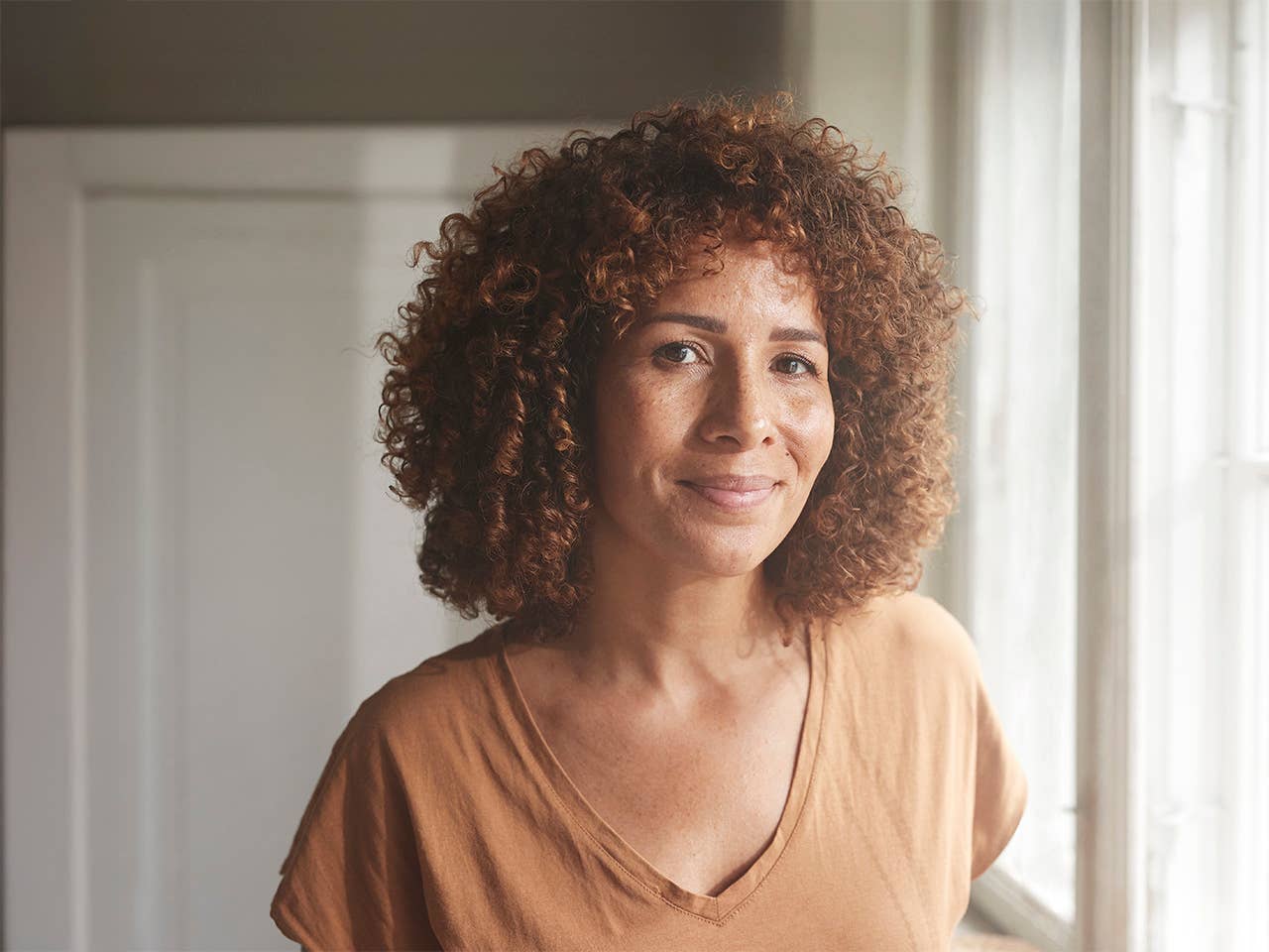 Smiling Black woman with curly brown hair stands in a sunny room