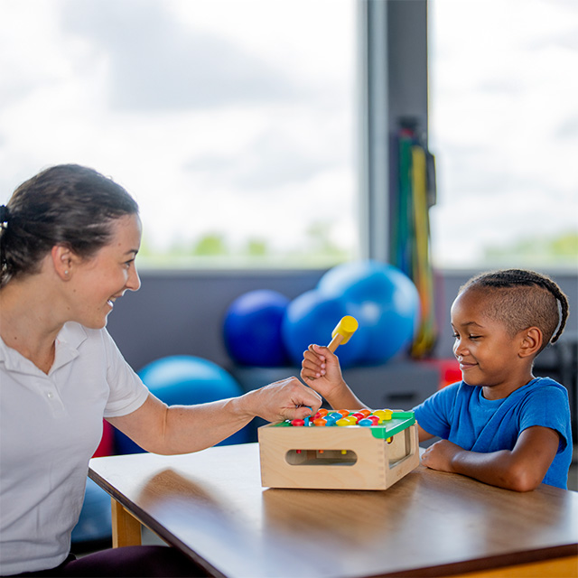 A smiling Corewell Health pediatric occupational therapist bumps fists with a young Black child in a southeast Michigan clinic