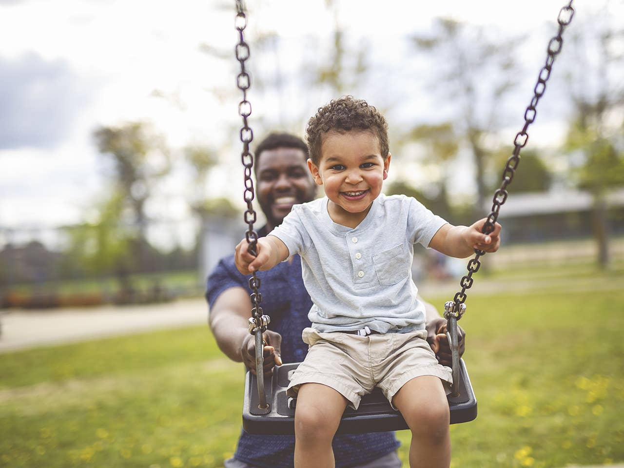 Father pushing his young son on a swing set at the park.