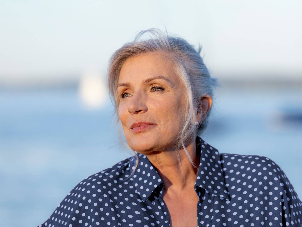 Older white woman with grey hair stands in front of a lake in the evening sun