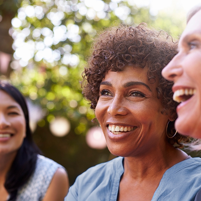 Three women laughing together outdoors, enjoying a sunny day and each other's company.