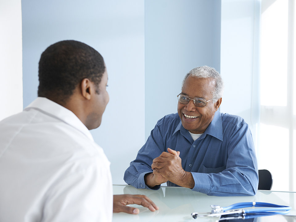 A man seated at a table engages in conversation with a physician.