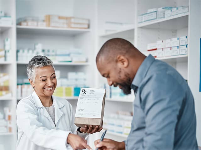 Smiling Corewell Health Specialty Pharmacy team member hands a paper bag containing a prescription to a smiling patient