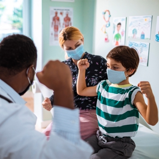 Young boy sitting in chair flexes his arms alongside a doctor