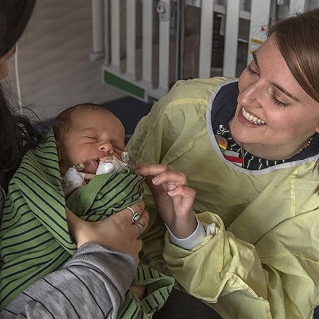 Mother holds baby while talking to a smiling doctor in the neuromuscular clinic