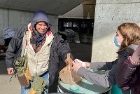 A man distributes food to individuals on the sidewalk, promoting community support and engagement in diverse neighborhoods.