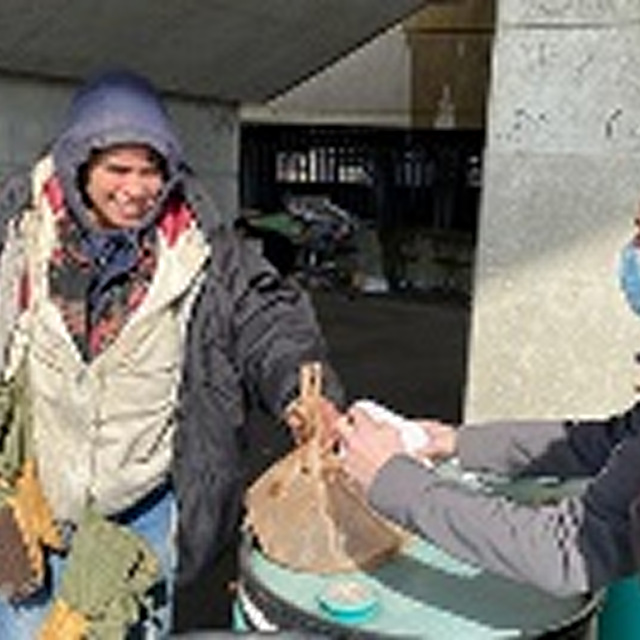 A man distributes food to individuals on the sidewalk, promoting community support and engagement in diverse neighborhoods.