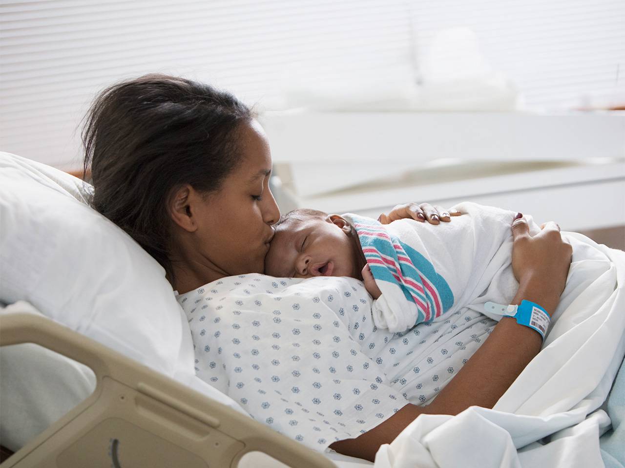Women laying in a hospital bed while holding her sleeping newborn baby