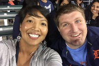 A man and woman smiling while taking a selfie at a baseball game, capturing a joyful moment together.
