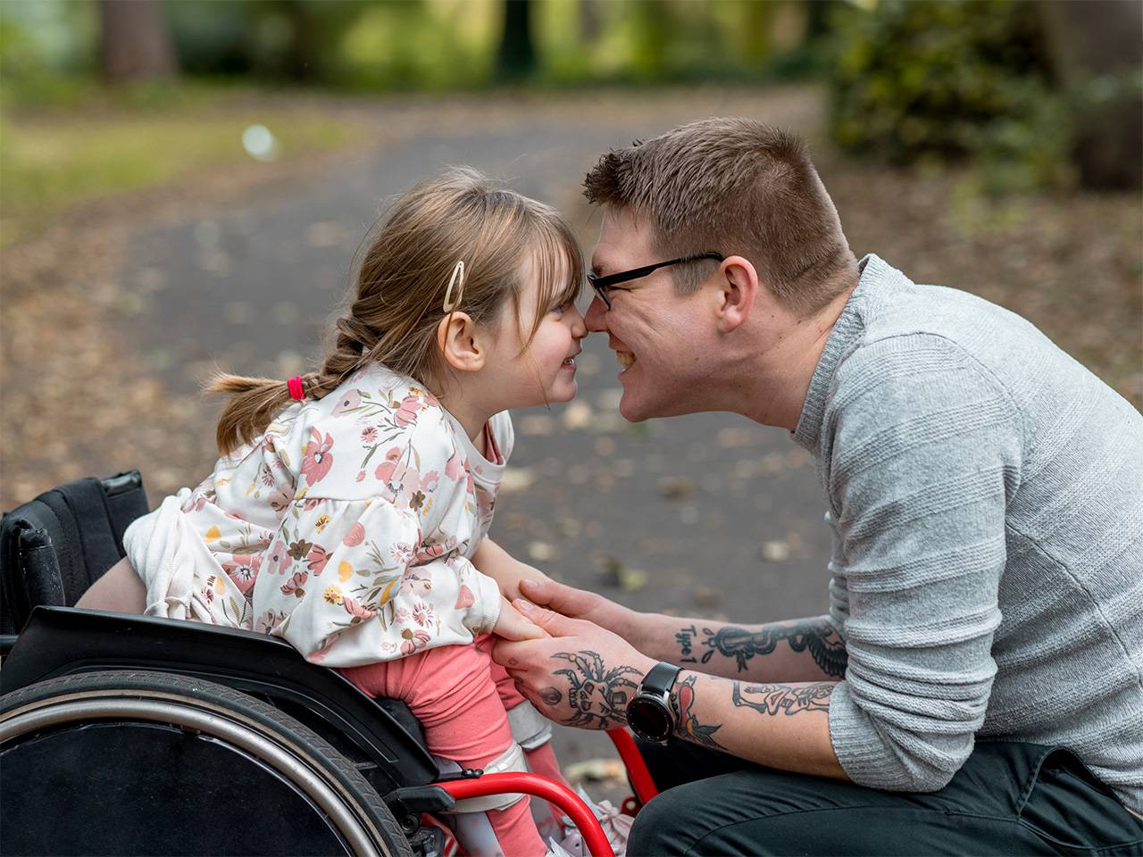 Smiling Black girl with curly brown hair holds on to her mother's back as she is carried in a park outdoors