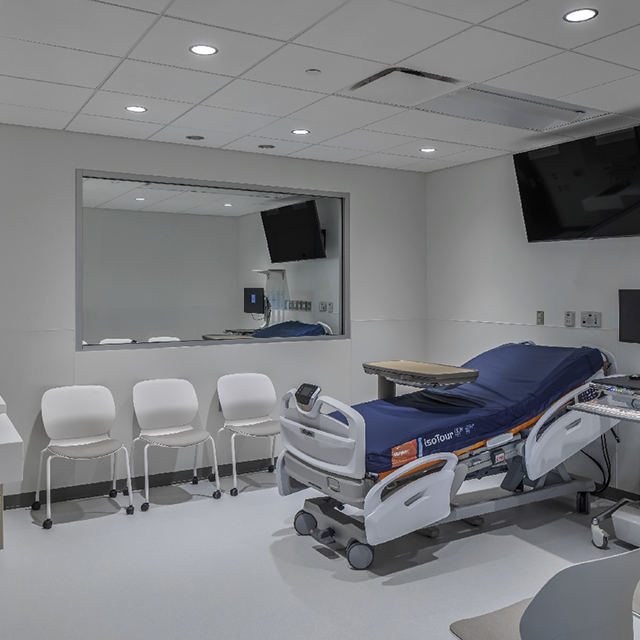 A hospital room with a bed, chairs, and a television, part of a training facility with various simulation labs and classrooms.